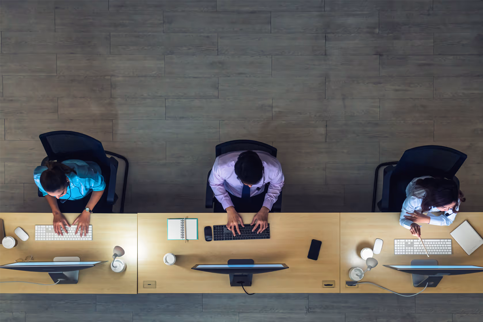 Three call center agents working at desks with computers, typing and wearing headsets.