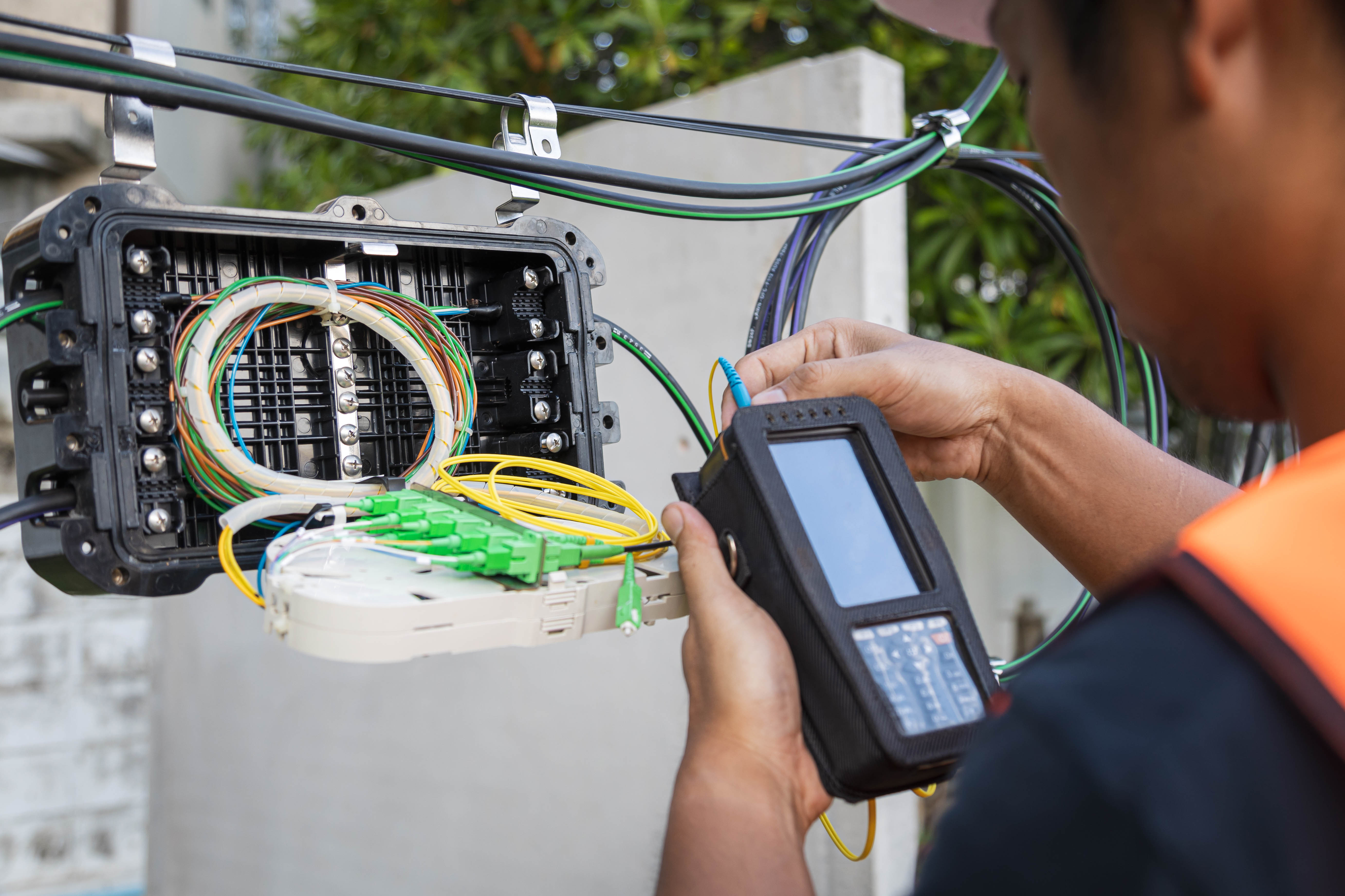 Technician testing fiber optic cables with a handheld device on an outdoor network box.