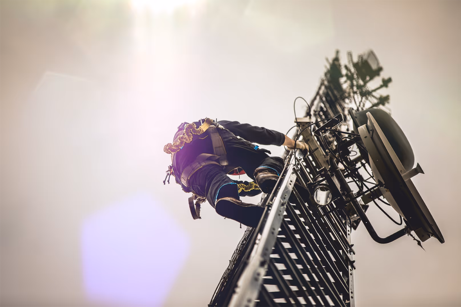 Technician climbing a telecommunication tower with safety gear to maintain network equipment.