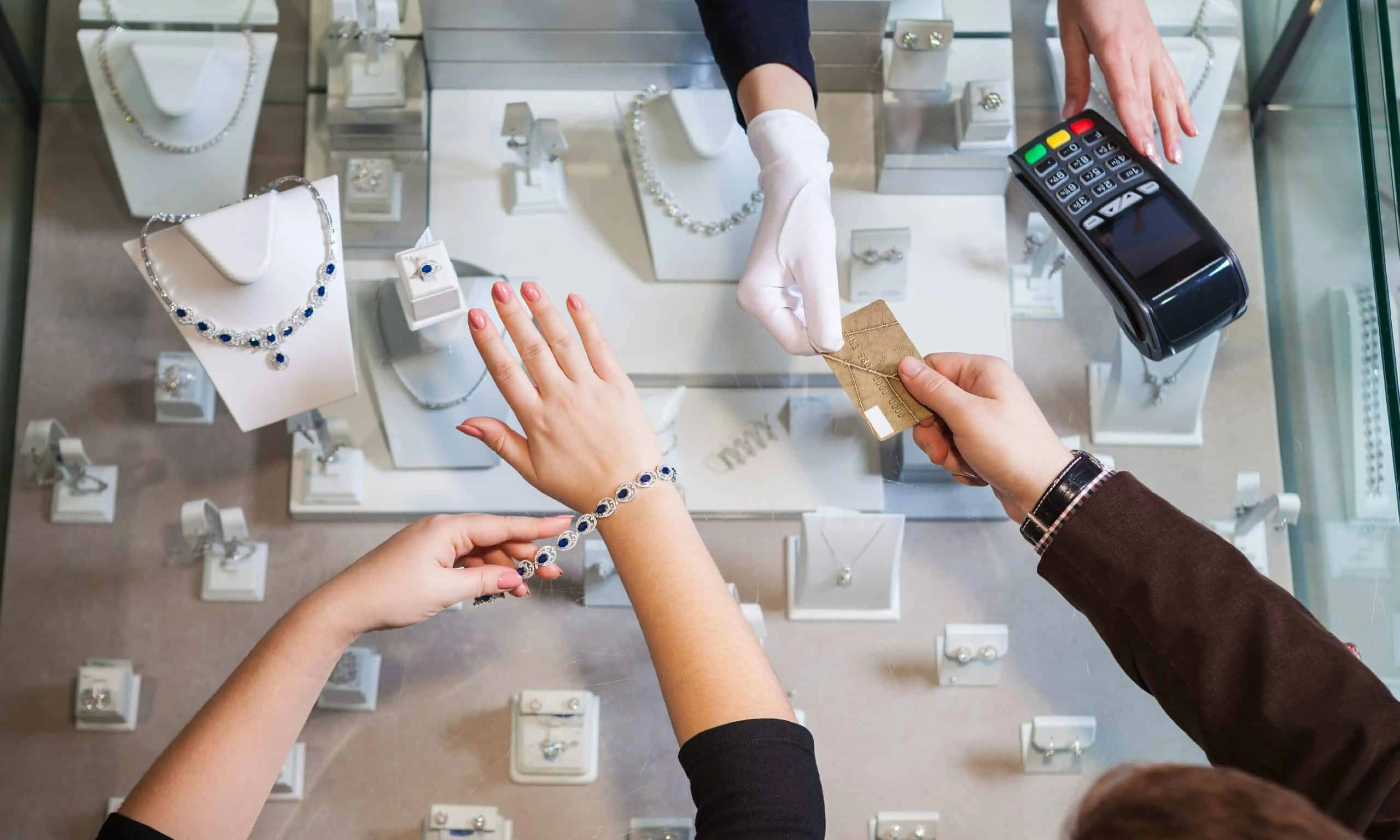 Customer tries sapphire jewelry bracelet at store while paying with card to clerk wearing white gloves.